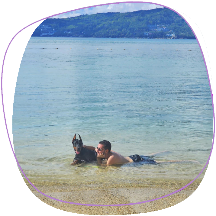 Doberman At The Beach In Phuket With His Owner Hagging In The Sea